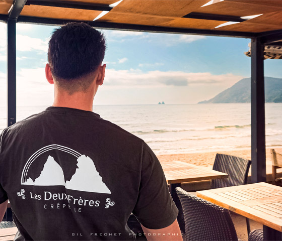 Crêpier des Deux Frères de dos, tee-shirt au logo de la crêperie, contemplant la mer depuis la terrasse des Sablettes